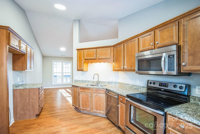 kitchen with vaulted ceiling, stainless steel appliances, light wood-type flooring, light stone countertops, and sink