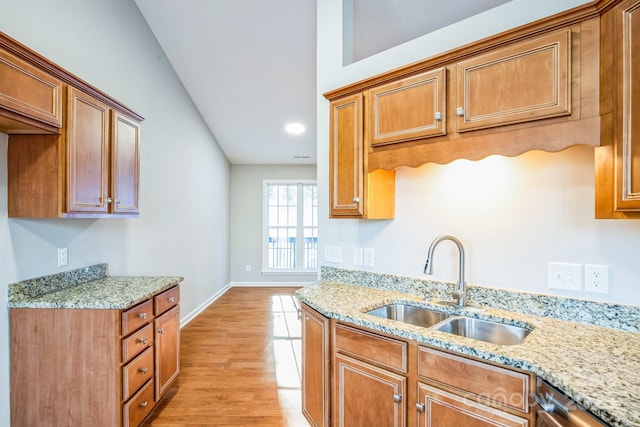 kitchen featuring sink, vaulted ceiling, light hardwood / wood-style floors, stainless steel dishwasher, and light stone countertops