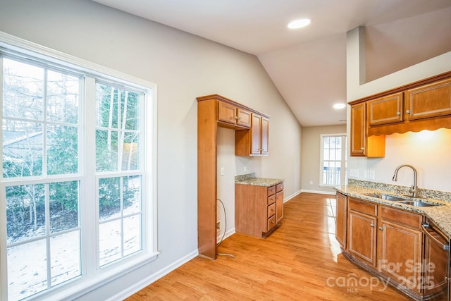 kitchen with vaulted ceiling, light stone counters, sink, light hardwood / wood-style flooring, and stainless steel dishwasher