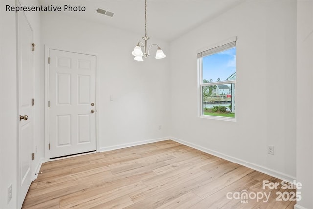 empty room featuring a notable chandelier and light hardwood / wood-style flooring