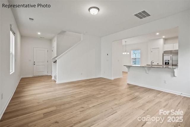 unfurnished living room featuring light hardwood / wood-style floors, a chandelier, and sink