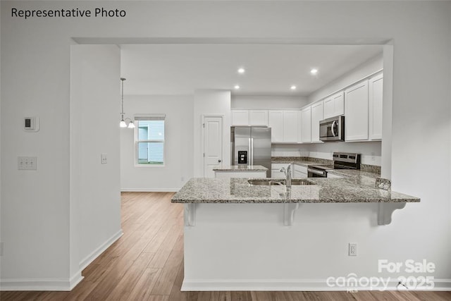 kitchen featuring stainless steel appliances, hanging light fixtures, kitchen peninsula, a breakfast bar, and white cabinets