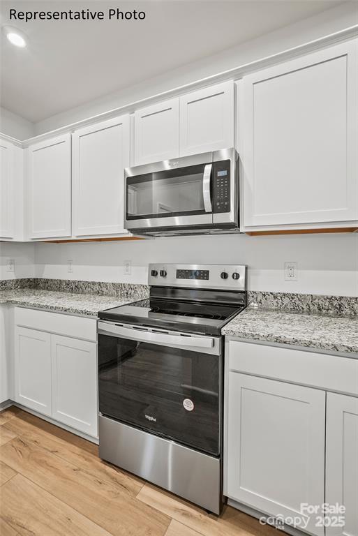 kitchen featuring white cabinetry, light wood-type flooring, light stone counters, and appliances with stainless steel finishes