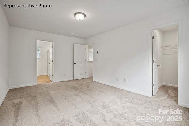 unfurnished bedroom featuring a spacious closet, a closet, ensuite bath, multiple windows, and light colored carpet