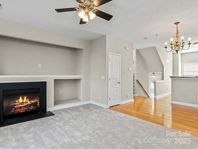 unfurnished living room featuring built in features, ceiling fan with notable chandelier, and light colored carpet