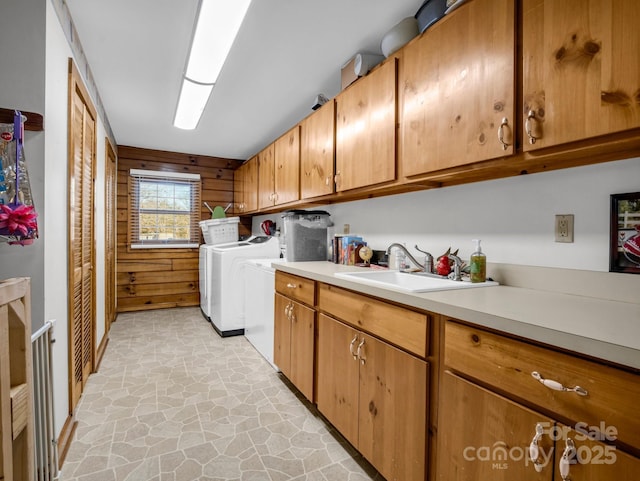 laundry area featuring cabinets, sink, wooden walls, and independent washer and dryer