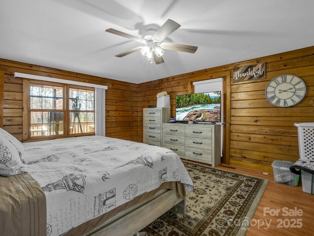 bedroom featuring light wood-type flooring, ceiling fan, and wood walls