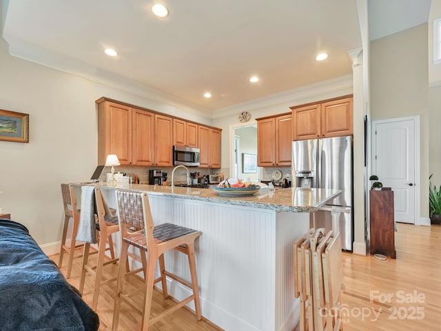 kitchen with stainless steel appliances, light stone countertops, kitchen peninsula, and a breakfast bar area