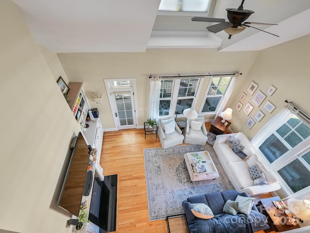 living room with a towering ceiling, ceiling fan, and light wood-type flooring