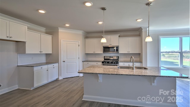 kitchen featuring stainless steel appliances, sink, decorative light fixtures, white cabinets, and a center island with sink