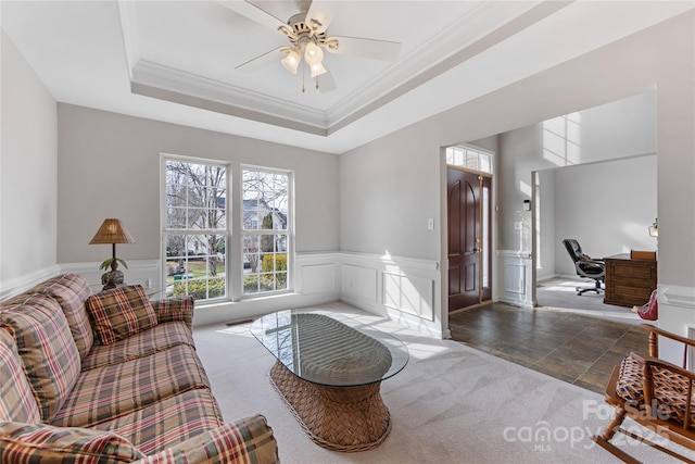 carpeted living room with a tray ceiling, ornamental molding, and ceiling fan