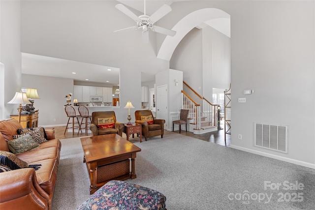 carpeted living room with ceiling fan and a high ceiling