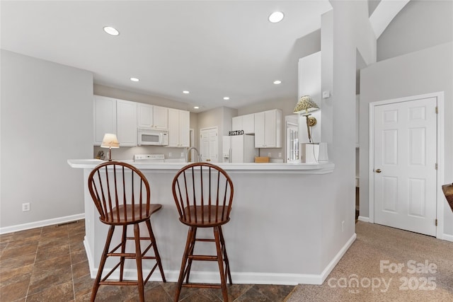 kitchen with sink, a breakfast bar area, white cabinets, kitchen peninsula, and white appliances