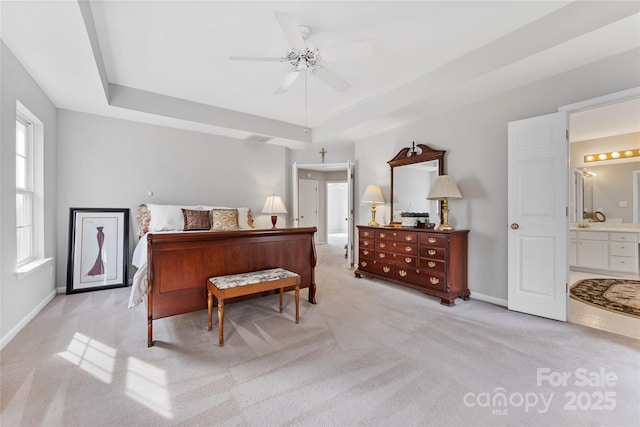 bedroom with ensuite bathroom, a raised ceiling, and light carpet