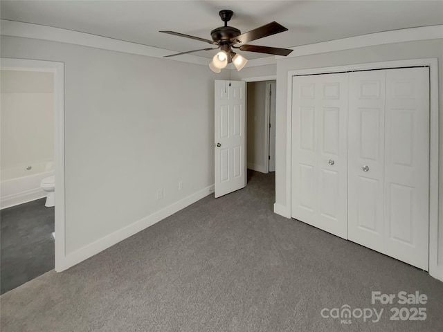 unfurnished bedroom with a closet, ensuite bath, ceiling fan, and dark carpet