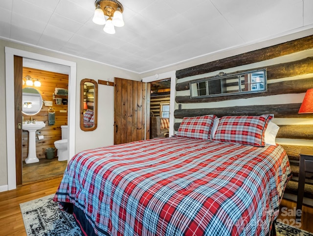 bedroom featuring connected bathroom, hardwood / wood-style floors, and wood walls