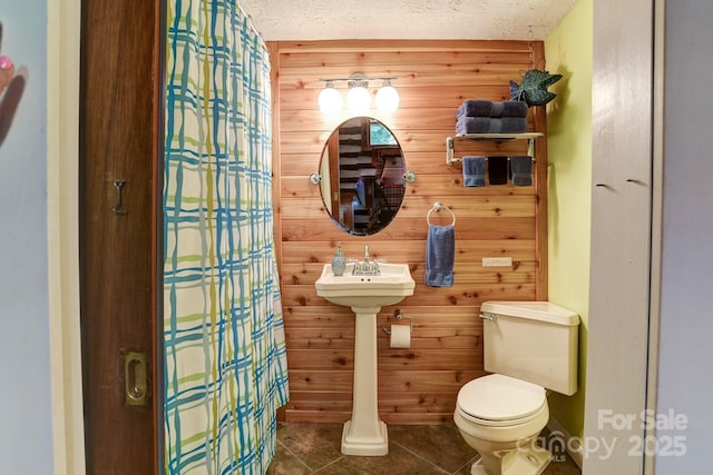 bathroom featuring a shower with curtain, toilet, a textured ceiling, and wood walls