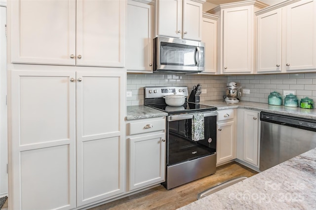 kitchen with light stone countertops, white cabinetry, stainless steel appliances, backsplash, and light wood-type flooring