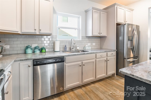 kitchen featuring light stone countertops, white cabinets, stainless steel appliances, sink, and light wood-type flooring