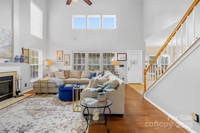 living room with ceiling fan, a fireplace, hardwood / wood-style floors, and a towering ceiling