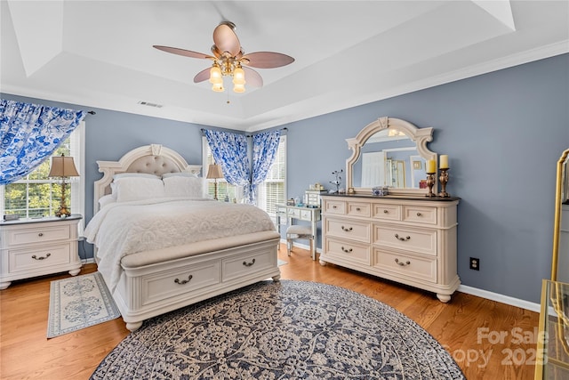 bedroom with light hardwood / wood-style flooring, a raised ceiling, and ceiling fan