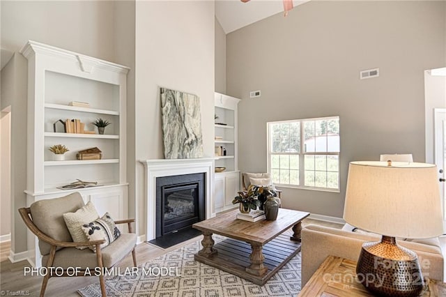 sitting room featuring high vaulted ceiling, built in shelves, light hardwood / wood-style flooring, and ceiling fan