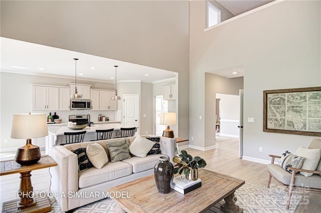 living room featuring a towering ceiling, ornamental molding, and light hardwood / wood-style flooring