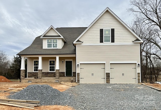 view of front of house featuring a garage, covered porch, stone siding, driveway, and roof with shingles