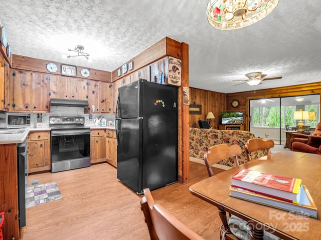 kitchen with appliances with stainless steel finishes, wooden walls, tasteful backsplash, light wood-type flooring, and a textured ceiling