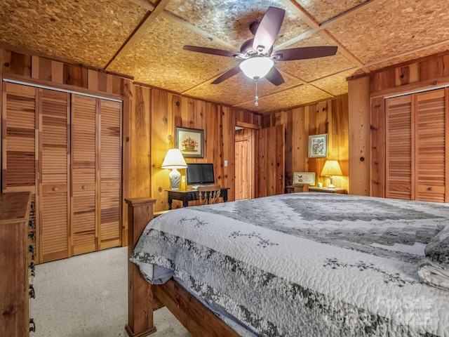 carpeted bedroom featuring two closets, wooden walls, and ceiling fan