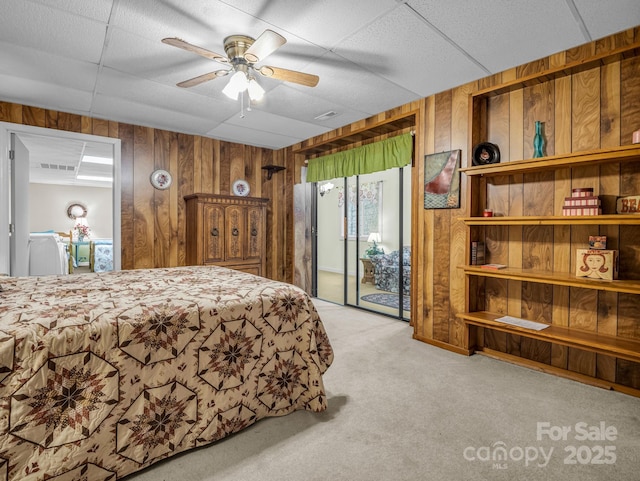 carpeted bedroom featuring ceiling fan, a drop ceiling, access to exterior, and wooden walls