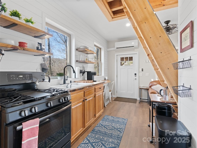 kitchen with sink, gas stove, a wall mounted AC, light hardwood / wood-style flooring, and dishwashing machine