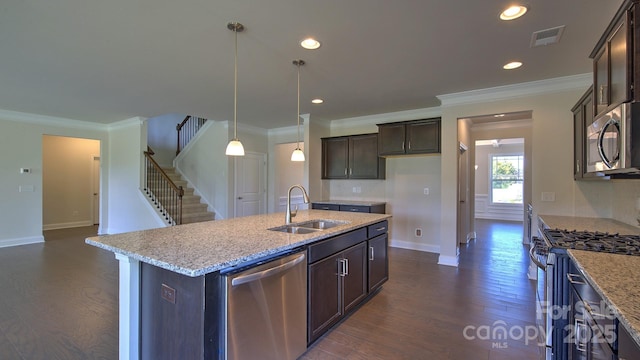 kitchen with stainless steel appliances, sink, decorative light fixtures, light stone countertops, and a kitchen island with sink