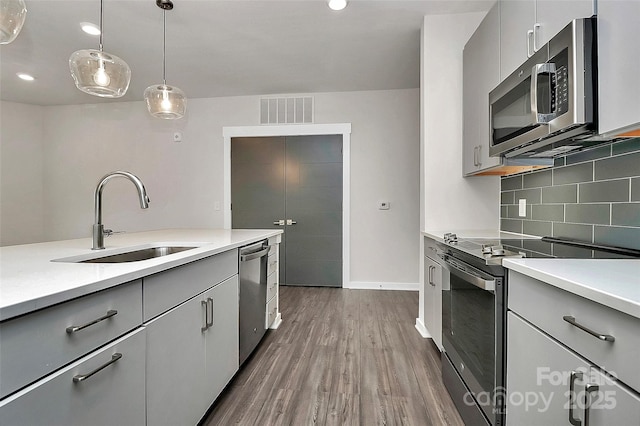 kitchen featuring decorative light fixtures, stainless steel appliances, decorative backsplash, sink, and gray cabinets