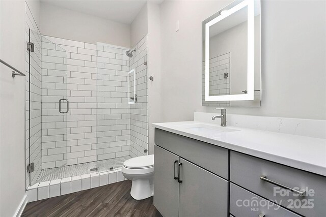 bathroom with hardwood / wood-style flooring, toilet, vanity, and a shower with shower door