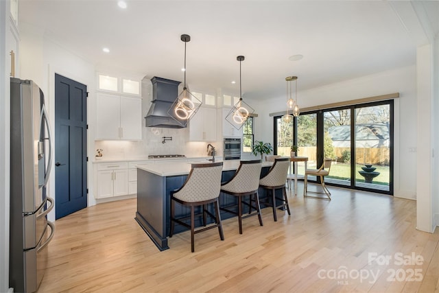 kitchen featuring white cabinets, appliances with stainless steel finishes, an island with sink, and premium range hood