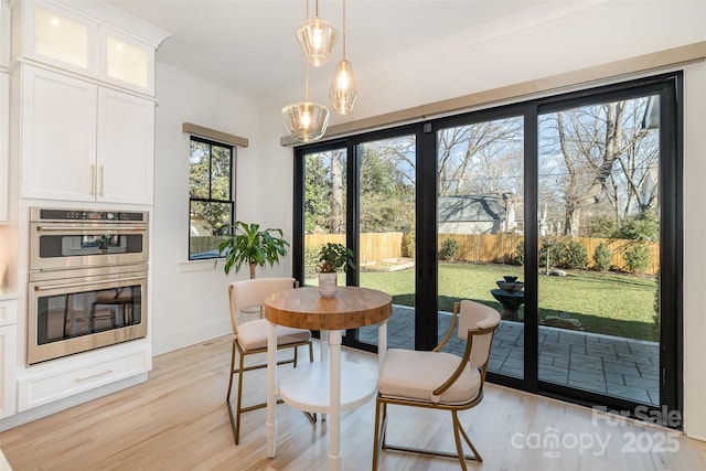 dining space with light wood-type flooring, crown molding, and a healthy amount of sunlight