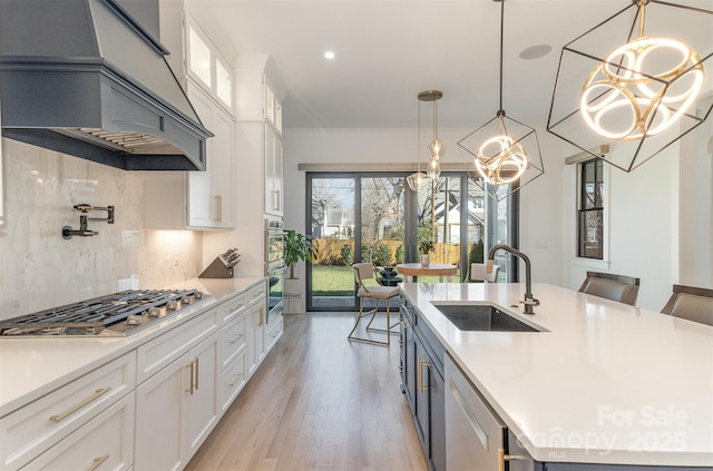 kitchen with custom exhaust hood, appliances with stainless steel finishes, decorative light fixtures, white cabinets, and sink