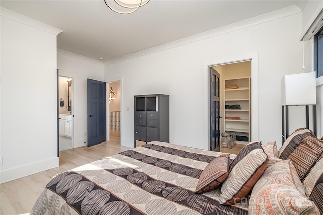 bedroom with a walk in closet, crown molding, light hardwood / wood-style floors, and ensuite bath