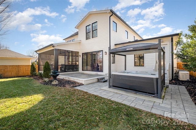 rear view of property featuring a patio area, a hot tub, a lawn, and a sunroom