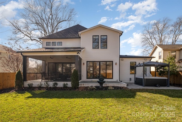 back of house featuring ceiling fan, a sunroom, a yard, a hot tub, and a patio