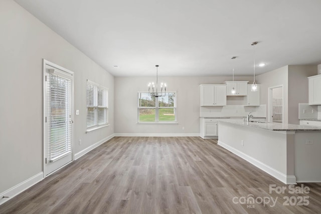 interior space with light stone counters, light hardwood / wood-style flooring, hanging light fixtures, white cabinetry, and sink