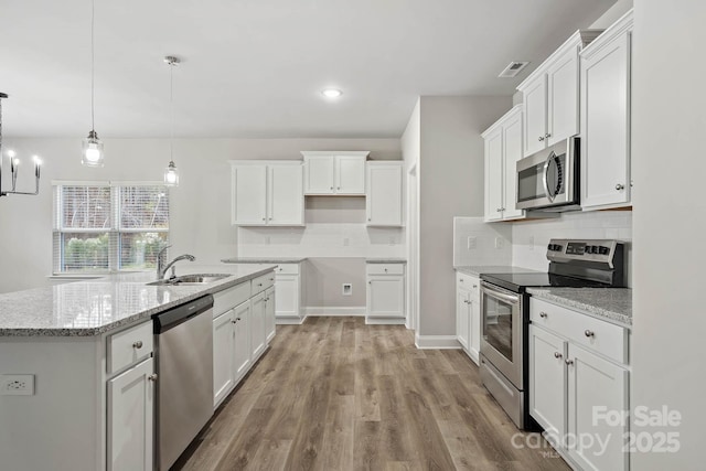 kitchen with appliances with stainless steel finishes, hanging light fixtures, light stone countertops, white cabinets, and sink