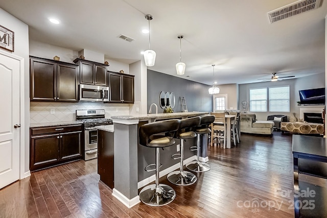 kitchen featuring dark brown cabinetry, stainless steel appliances, backsplash, hanging light fixtures, and a breakfast bar