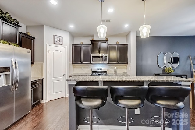 kitchen with appliances with stainless steel finishes, a kitchen island, decorative light fixtures, dark wood-type flooring, and decorative backsplash