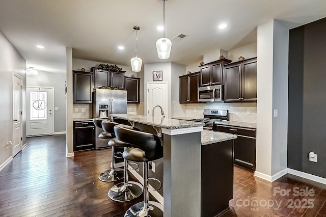 kitchen with pendant lighting, a breakfast bar, decorative backsplash, appliances with stainless steel finishes, and an island with sink