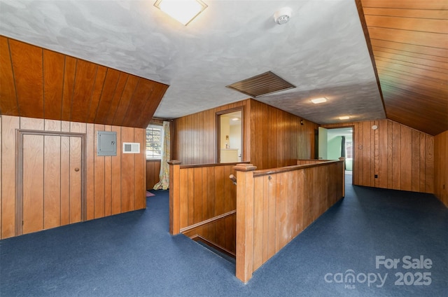 additional living space with lofted ceiling, electric panel, wooden walls, a textured ceiling, and dark colored carpet