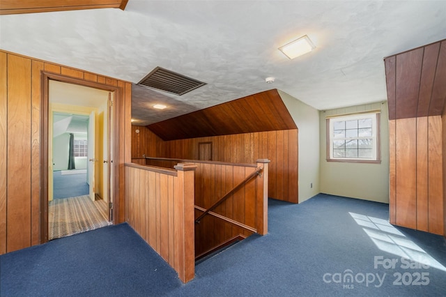 bonus room with vaulted ceiling, carpet flooring, a textured ceiling, and wood walls