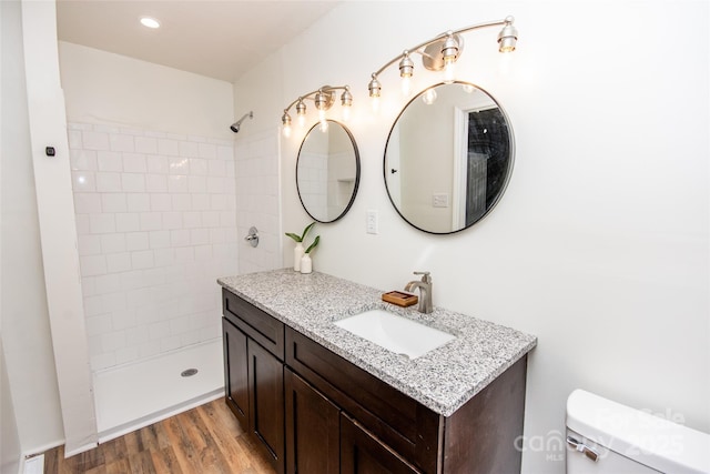 bathroom featuring toilet, vanity, wood-type flooring, and a tile shower