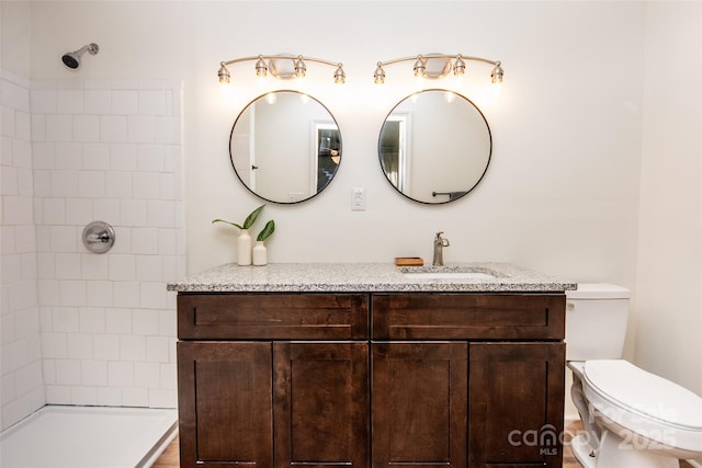 bathroom featuring toilet, vanity, and tiled shower